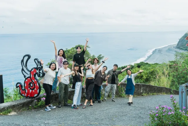 A group of about ten people pose cheerfully at a coastal overlook with ocean and cliffs behind them