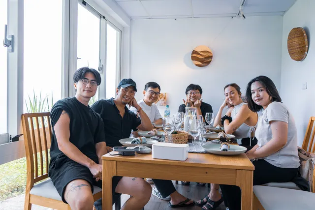 Six friends smiling together at a dining table in a bright cafe