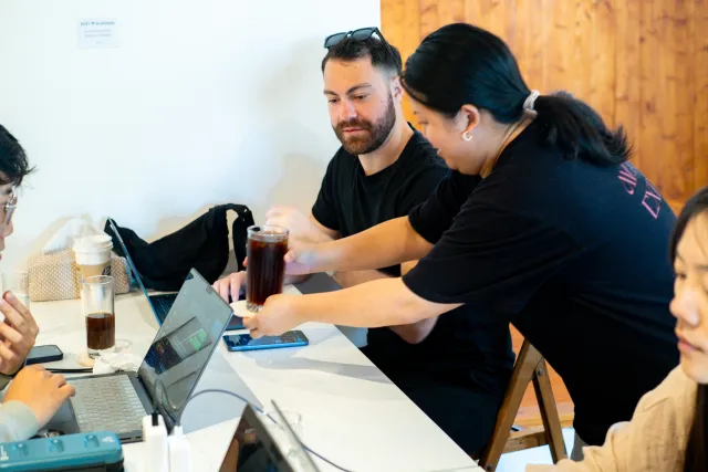 Two people collaborating over a laptop at a bright café table with iced drinks