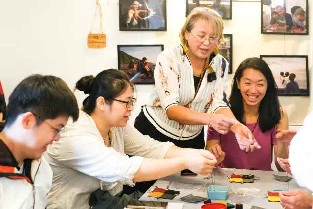 An instructor guides three seated participants in a hands-on craft workshop indoors