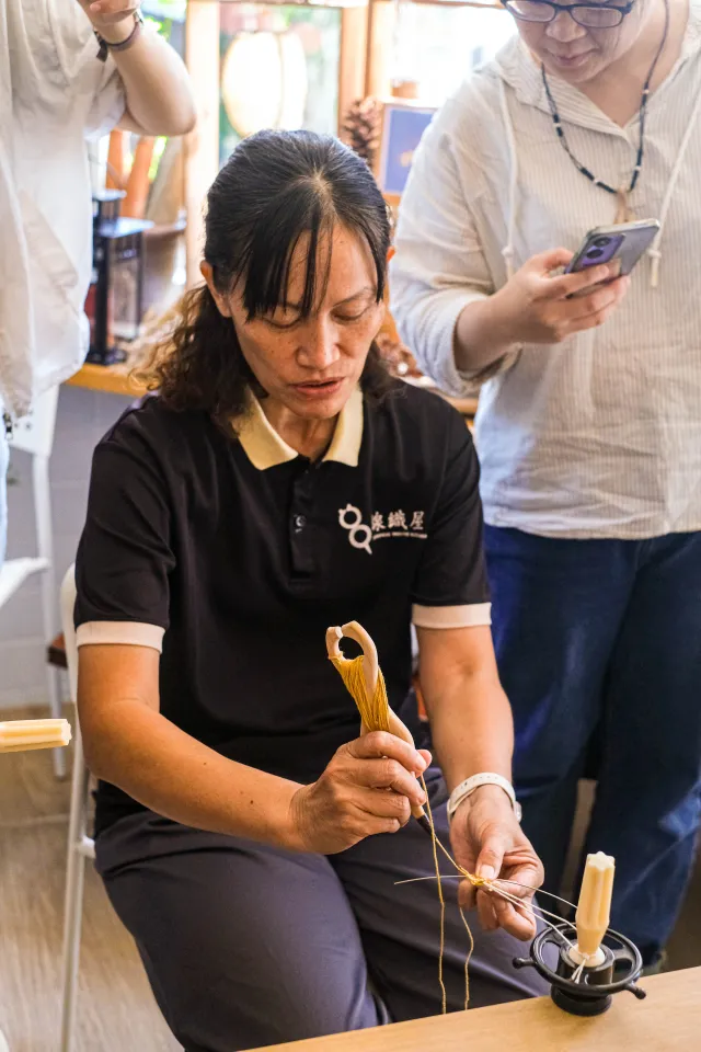 A craft instructor concentrates while hand-stitching dried grass into a figurine at an indoor workshop