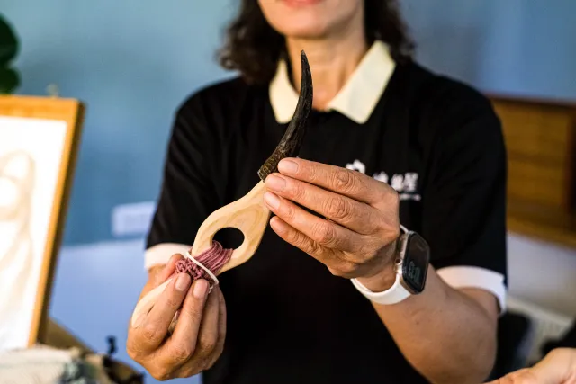 Instructor holds a wooden tool threaded with pink cord during a craft workshop