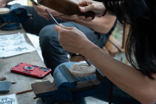 A participant carefully engraves a design onto a small wooden piece held in a bench vise