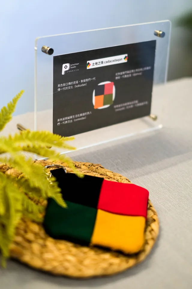 Colorful patchwork fabric craft piece displayed on a woven tray beside an explanatory sign
