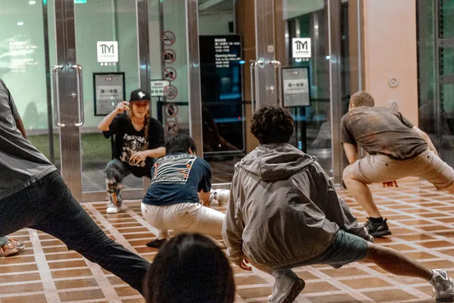 Several people crouch low in a hip-hop dance drill outside a museum entrance at night