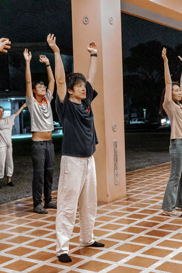 participants raising both arms during an outdoor hip-hop dance workshop at night