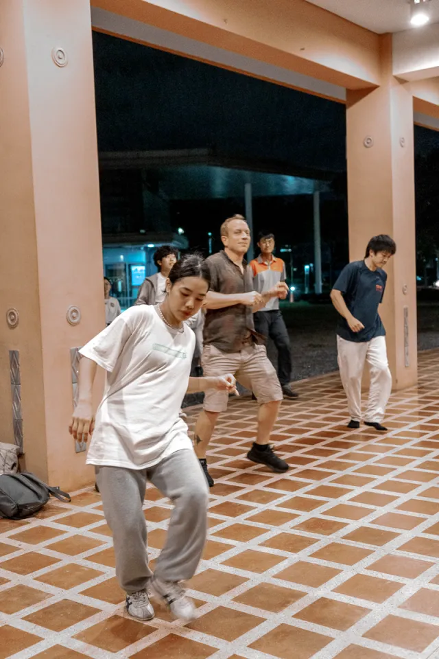A group of people practicing hip-hop dance moves together on a covered outdoor plaza at night