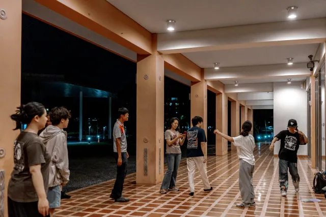 Young people gathered in an open corridor at night, some dancing and gesturing