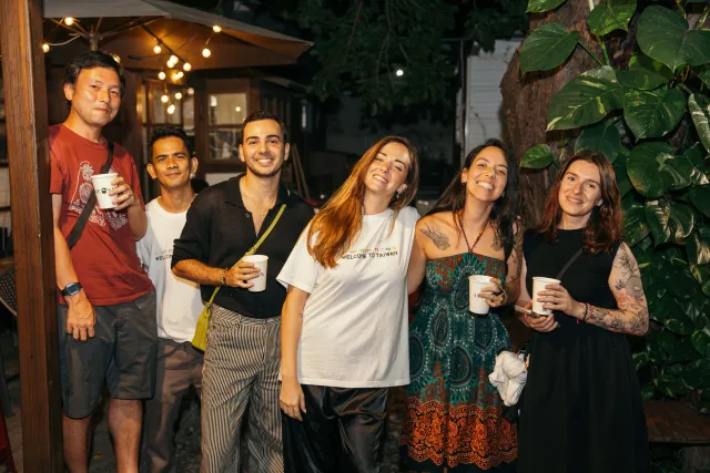 six smiling attendees holding cups pose together outdoors at a nighttime jazz event