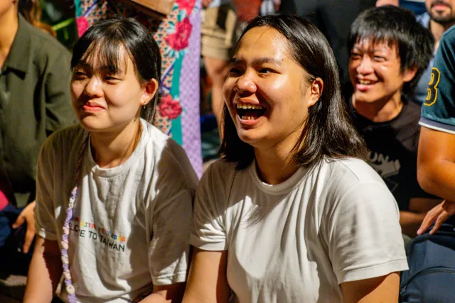 Two young women laugh and smile while seated at an outdoor event