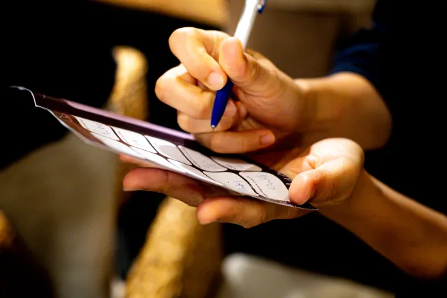A hand writing on a small booklet with a blue pen in a dimly lit setting