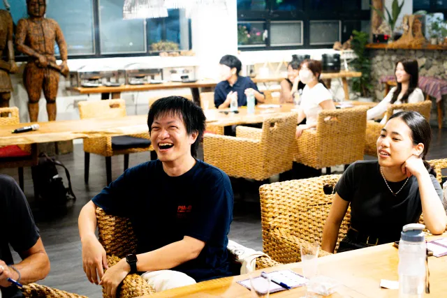 Two young people laugh and smile while seated at tables in a cafe gathering
