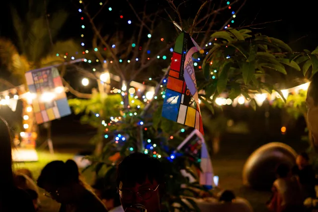 Crowd gathers at an outdoor night market under colorful string lights and decorated trees