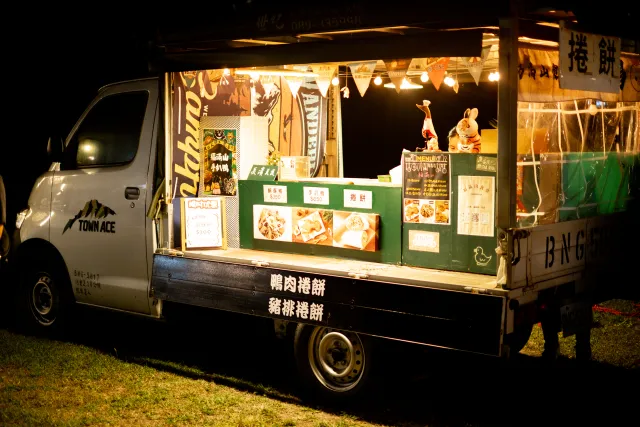 A food truck selling duck and pork wraps lit up at night in an open field