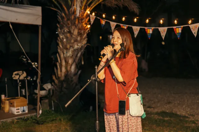 A woman in a red top speaks into a microphone at an outdoor night market