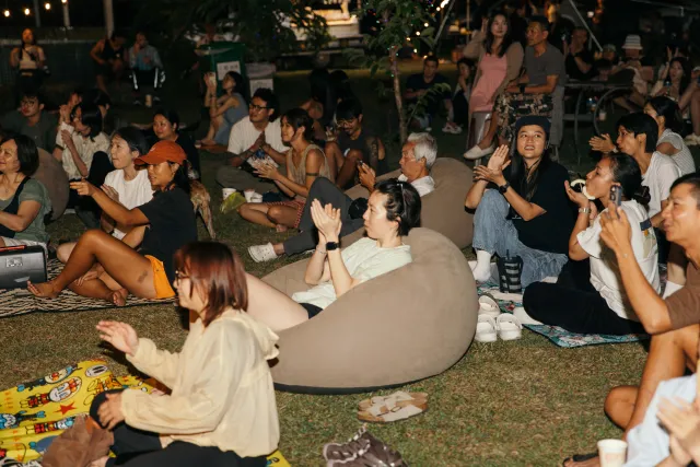 crowd seated on grass at night clapping and watching an outdoor event