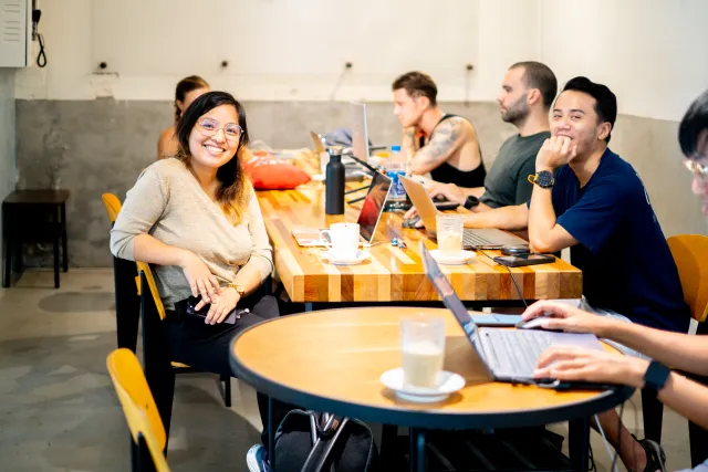 participants working on laptops in a casual cafe, smiling at the camera
