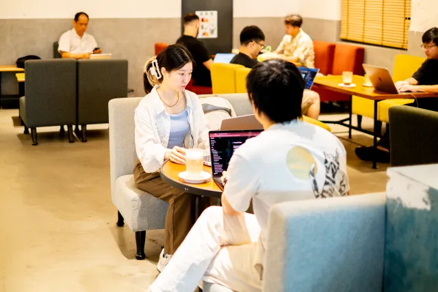Two attendees converse over laptops and coffee in a modern co-working lounge