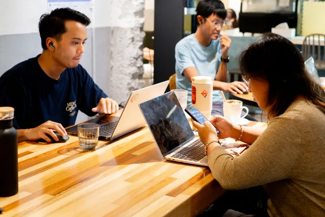 Three people working on laptops and a phone at a wooden cafe table
