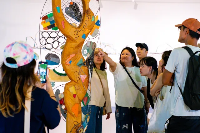 Visitors gather around a colorful sculpted tree artwork inside a gallery