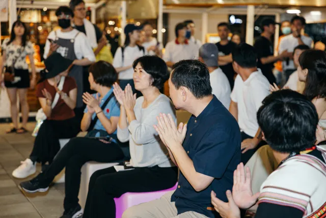 Seated audience members clapping at an indoor evening event