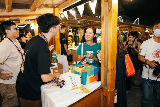 A smiling vendor chats with attendees at a lively outdoor night market booth