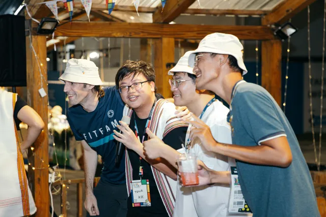 Four attendees wearing bucket hats laugh together at an indoor festival market booth