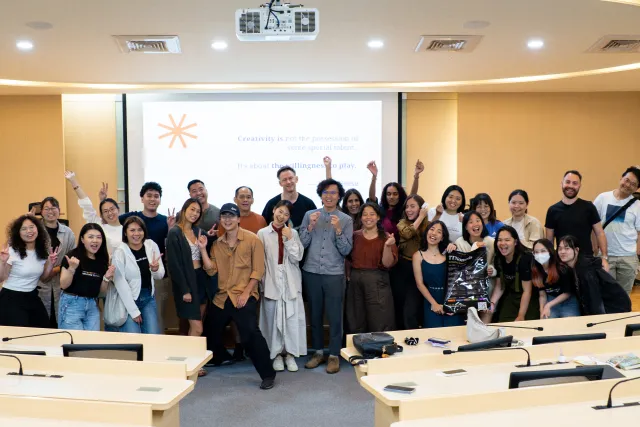 A large group of workshop participants pose cheerfully in a seminar room in front of a projection screen