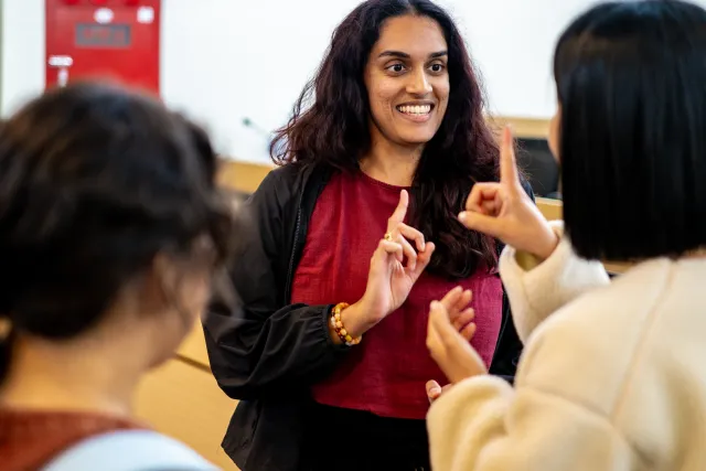 A smiling woman gestures with raised fingers while engaging two participants in a workshop discussion