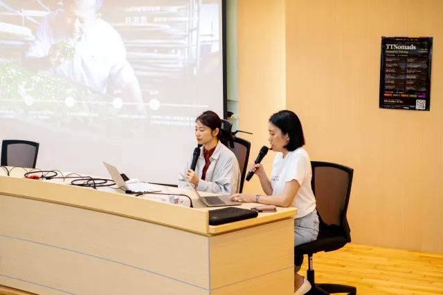 Two women co-present at a seminar table with a projected slide behind them