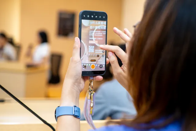 A woman holds up a smartphone displaying a Chinese-text interactive quiz screen indoors