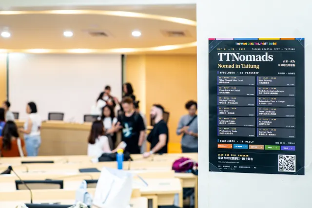 Event program poster in foreground with attendees mingling in a bright conference room behind