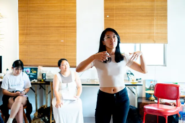 A woman gestures expressively while speaking to a small indoor audience