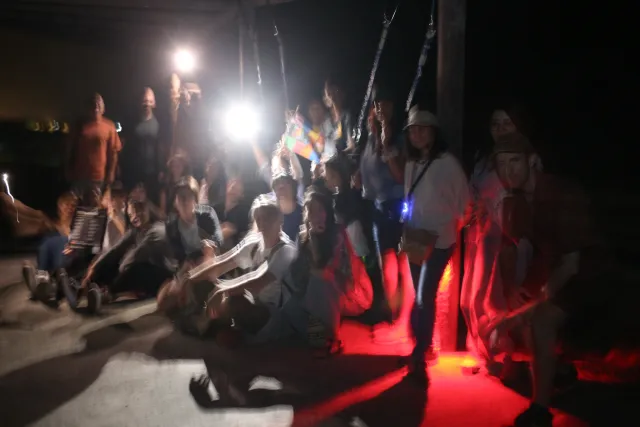A crowd of participants sitting and standing outdoors at night, raising hands under bright lights