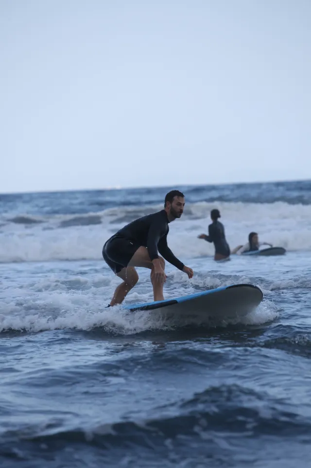 A surfer in a wetsuit rides a wave while two others paddle in the background