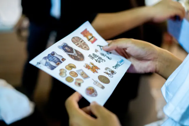 Two people examining a sheet of illustrated stickers at an indoor workshop