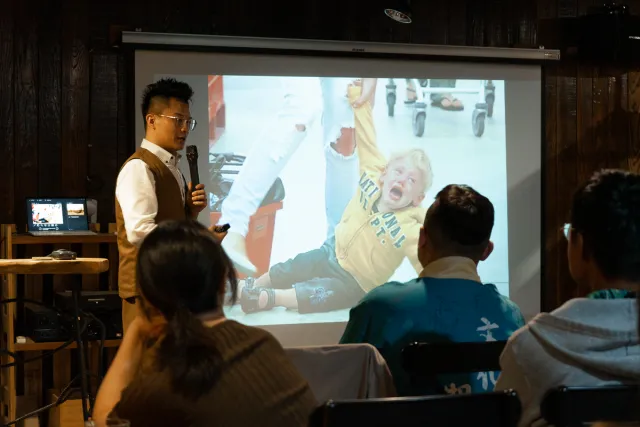 A speaker presents to a seated audience beside a projected image of a crying child