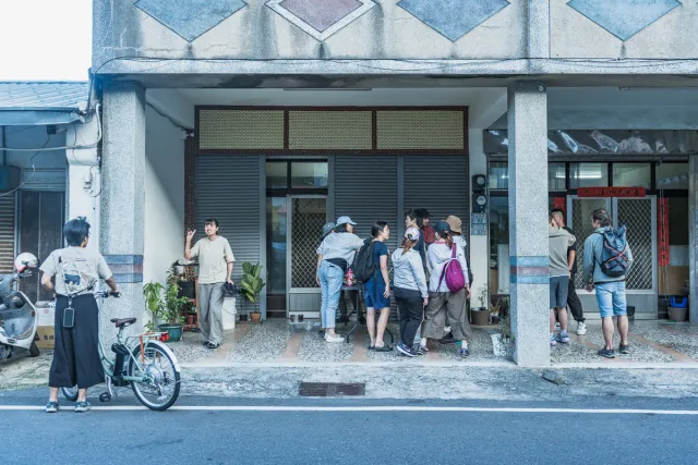 A group of visitors gathers on a covered sidewalk outside an old shophouse, listening to a local guide