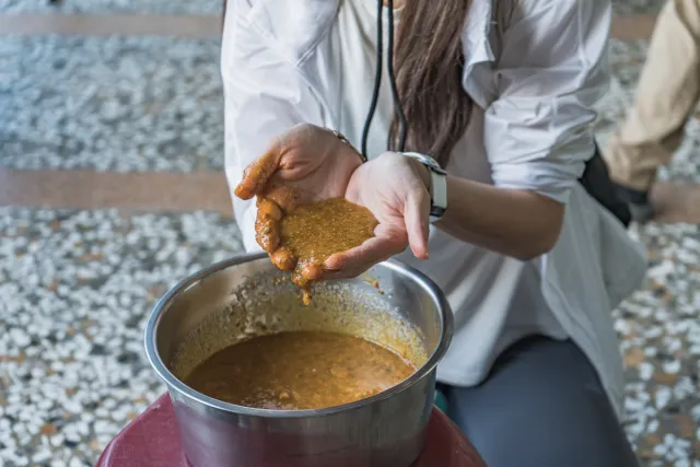 A woman kneads brown paste by hand over a metal bowl of sauce