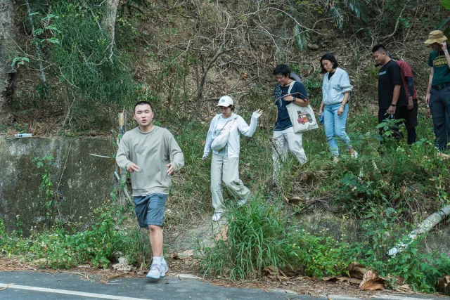 A group of visitors walks down a hillside trail onto a roadside in lush greenery