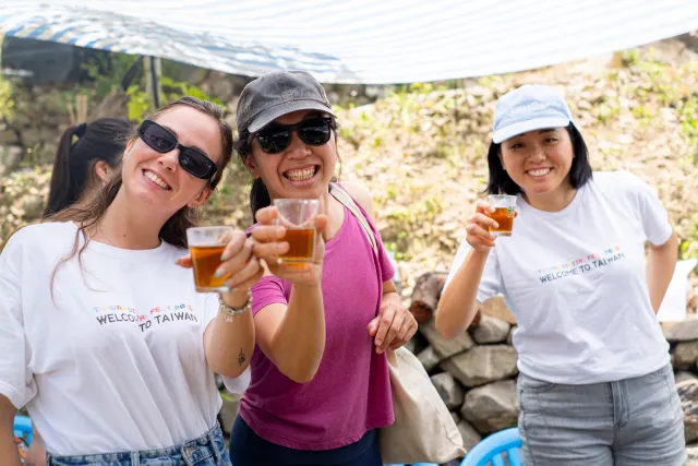 Three smiling women toast with small glasses of amber drink outdoors