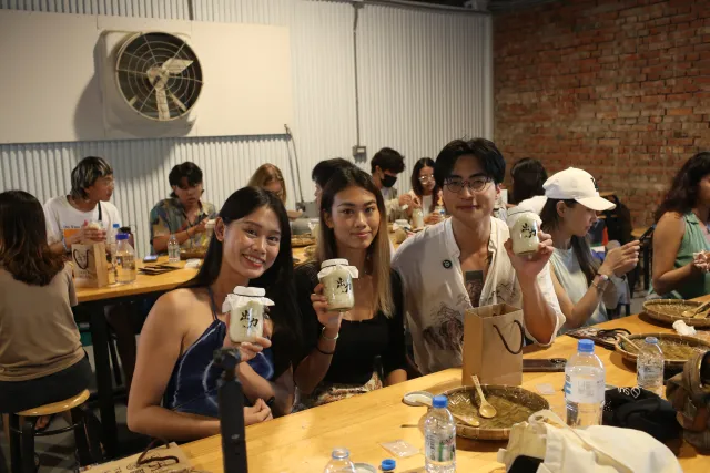Three young participants smile and hold up jars at a brewing workshop indoors