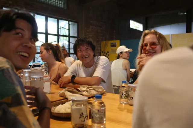 a group of young people laughing together at a long wooden table indoors