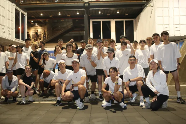 Large group of participants in white T-shirts posing together at night after a run event